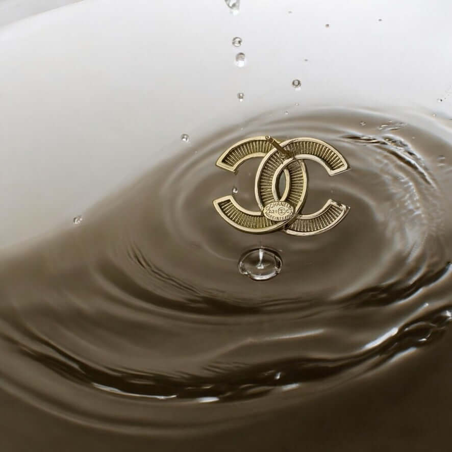 Chanel CC lighter gold earrings with pearls in rippling water background.