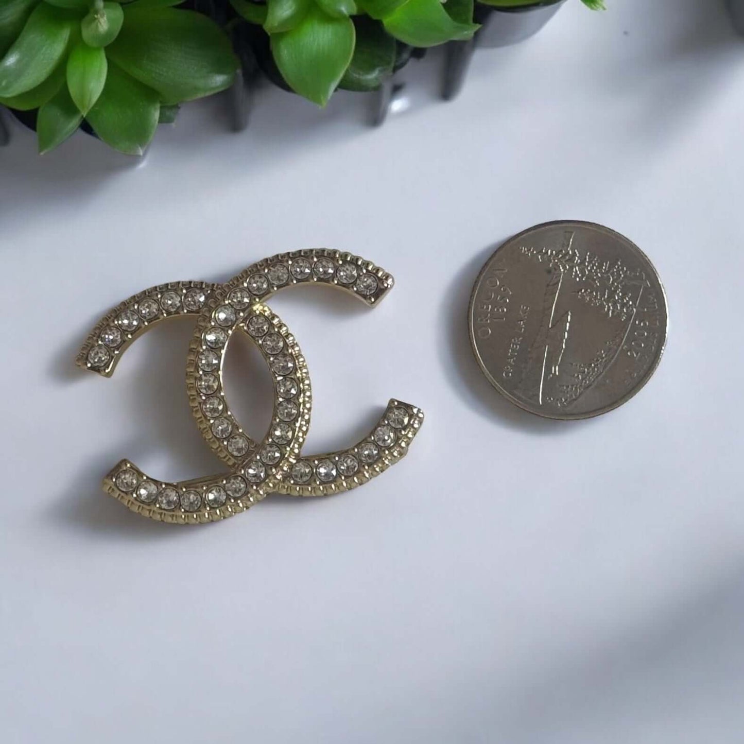 Stunning CHANEL Lighter Gold CC brooch with clear crystals, perfect for year-round wear, next to a coin for size reference.