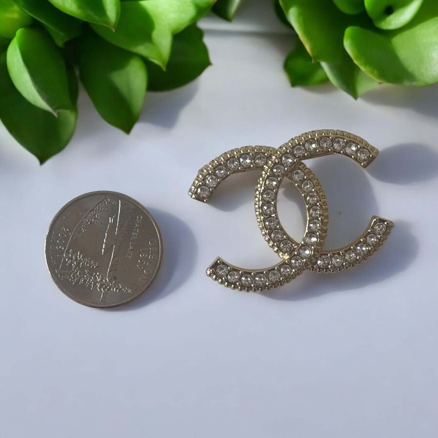 Stunning CHANEL Lighter Gold CC brooch with crystals, ideal for year-round wear, shown with a quarter for size reference.