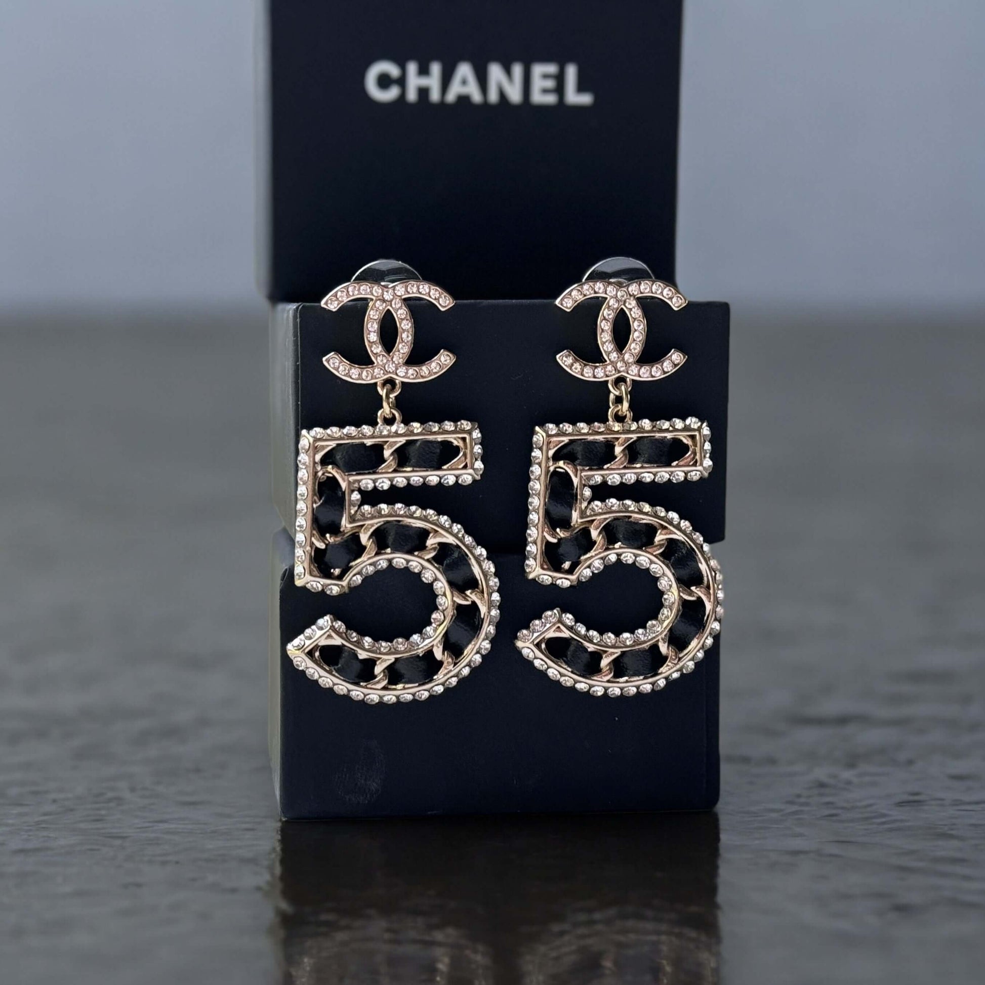 Chanel Gold Number 5 Big Dangle CC EarringsMake a statement with these iconic Chanel Gold Number 5 Big Dangle CC Earrings. The perfect addition to any outfit, these trendy and luxurious earrings feature gold plating, clear crystals, and a bold Chanel No.