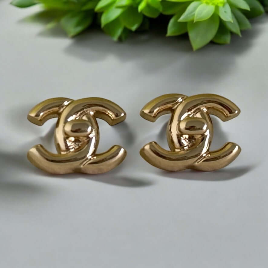 Chanel Gold CC Lock Smaller Post Earrings in Iconic Double C design, perfect for year-round wear, with greenery background.