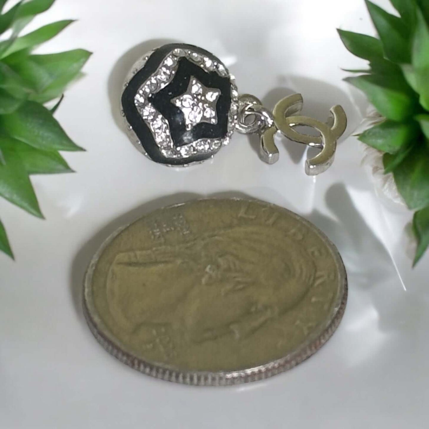 Chanel CC dangle earring with black enamel and silver star pattern next to a coin for size comparison.