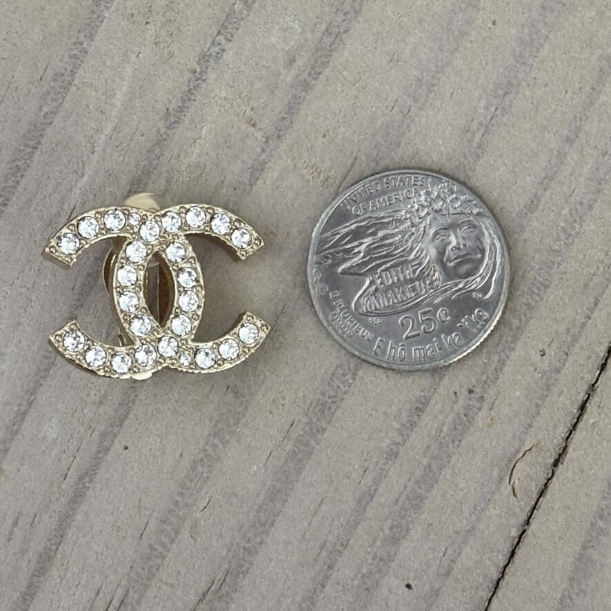 Authentic Chanel CC Lighter Gold Clip On Earrings with Crystals, featuring clear logo stamp, next to a quarter for size reference.