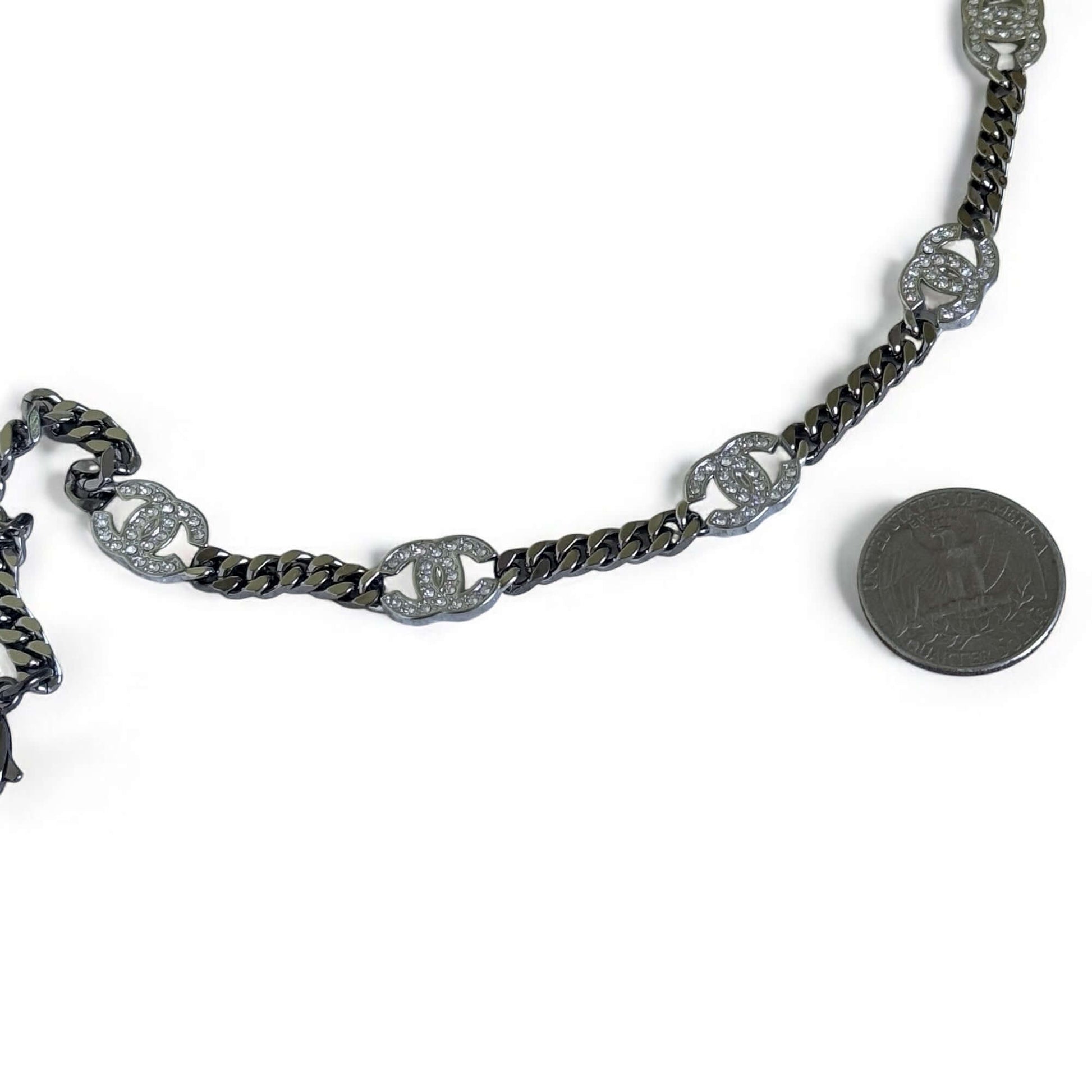 Authentic Chanel CC Choker in gunmetal, adjustable with crystal-encrusted CC's, alongside a coin for size reference.