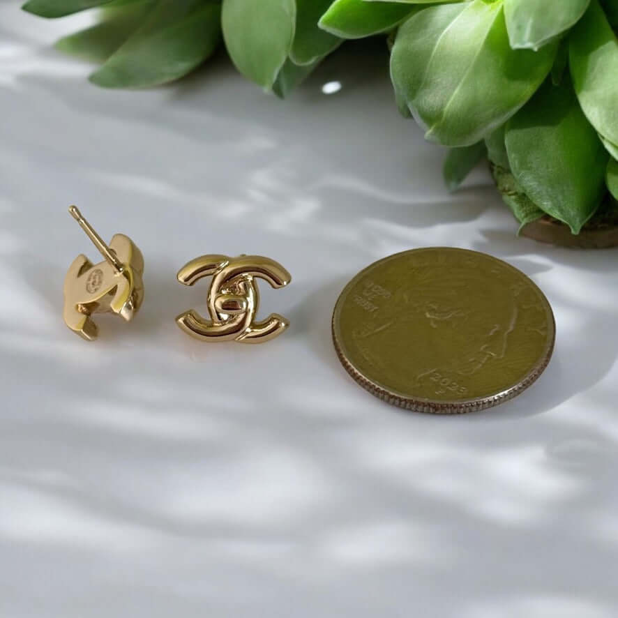 Chanel Gold CC Lock Smaller Post Earrings next to a coin for size comparison, showcasing iconic Double C design and gold plating.