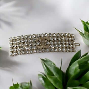 Chanel CC Gold Crystals Barette atop green leaves, featuring gold plating and clear crystals, showcasing luxury and elegance. My Mama Found What 