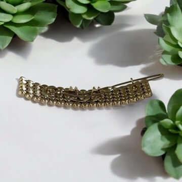 Chanel CC Gold Crystals Barette with clear crystals, authentic and pre-owned, displayed among green succulents. View details for Chanel CC Gold Crystals Barette.