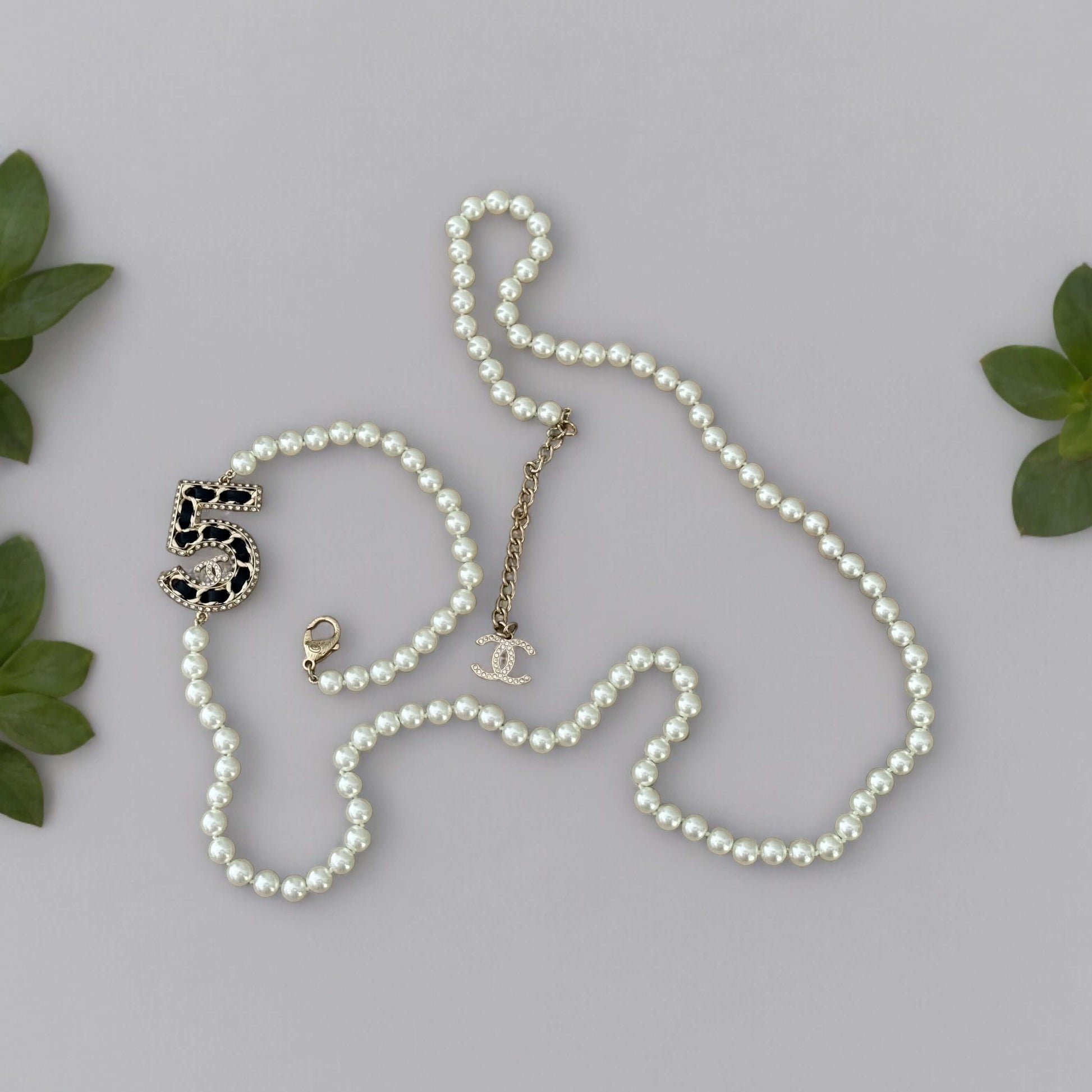 Chanel Knotted Pearl No.5 CC Sweater NecklaceIndulge in this gorgeous necklace adorned with a hand knotted pearl, Number 5 Chanel perfume charm, and sparkling crystals. The playful CC logo adds a touch of gold to the elegant black leather. Perfect for add