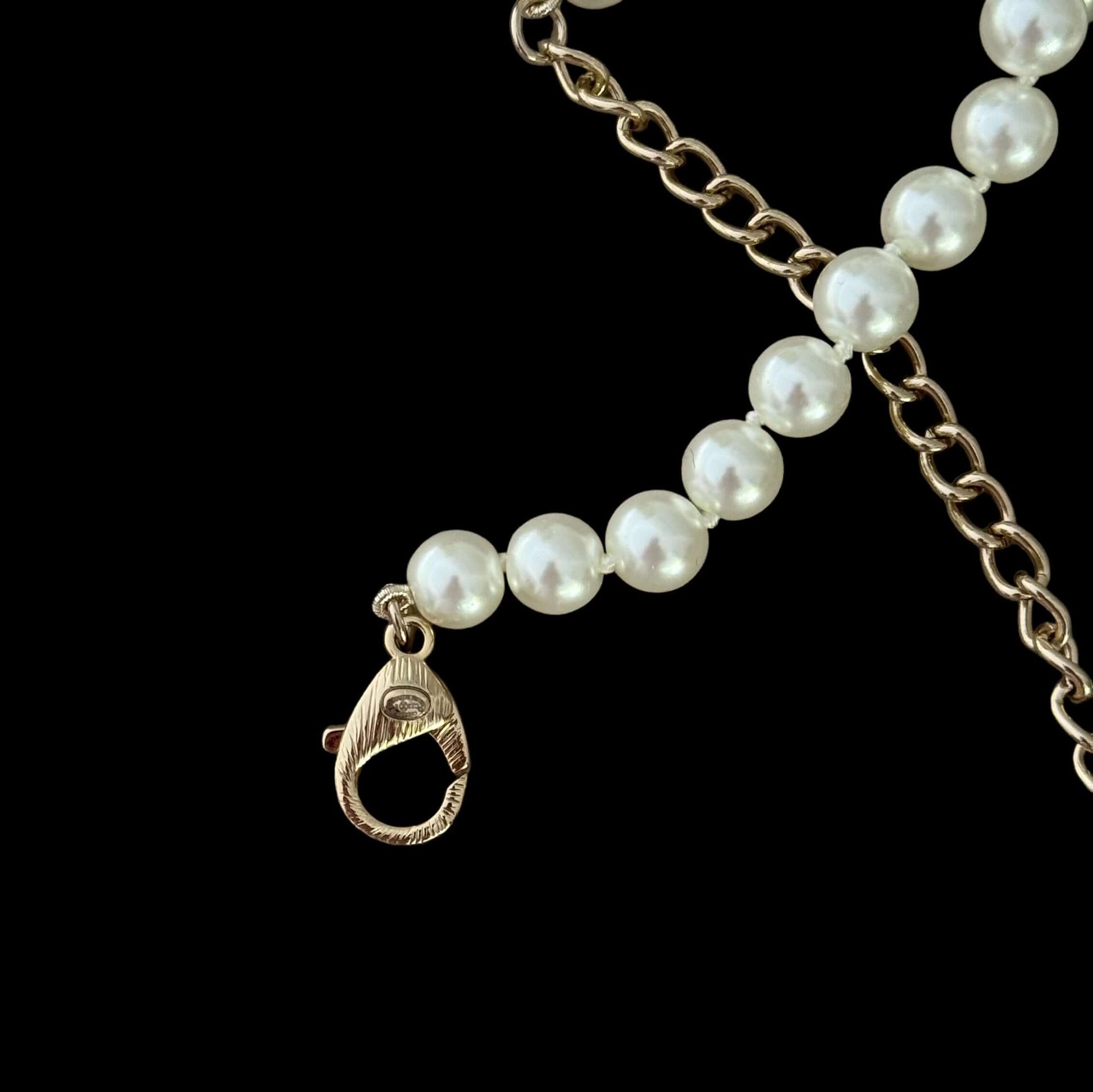 Chanel Knotted Pearl No.5 CC Sweater NecklaceIndulge in this gorgeous necklace adorned with a hand knotted pearl, Number 5 Chanel perfume charm, and sparkling crystals. The playful CC logo adds a touch of gold to the elegant black leather. Perfect for add