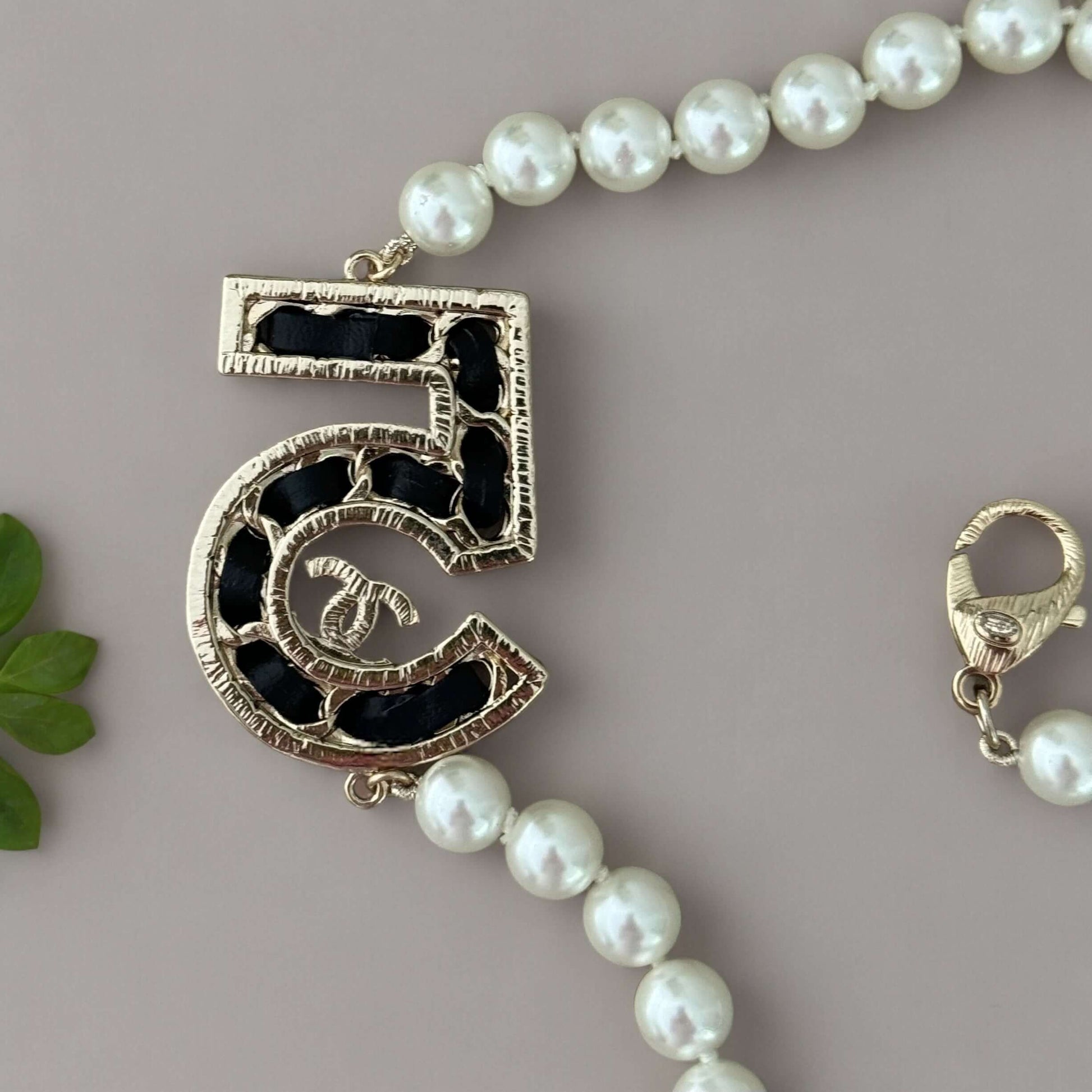 Chanel Knotted Pearl No.5 CC Sweater NecklaceIndulge in this gorgeous necklace adorned with a hand knotted pearl, Number 5 Chanel perfume charm, and sparkling crystals. The playful CC logo adds a touch of gold to the elegant black leather. Perfect for add