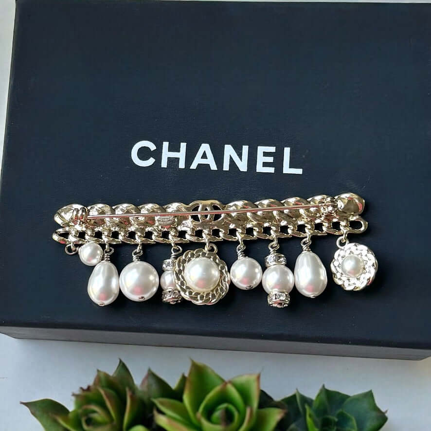 Chanel Rare Lighter Gold Long with Various Dangling Charms Brooch Pin 21 PIntroducing an elegant and rare brooch from Chanel, the Rare Lighter Gold Long Brooch with Various Dangling Charms! Accented with faux pearls and crystals, this brooch features a mi