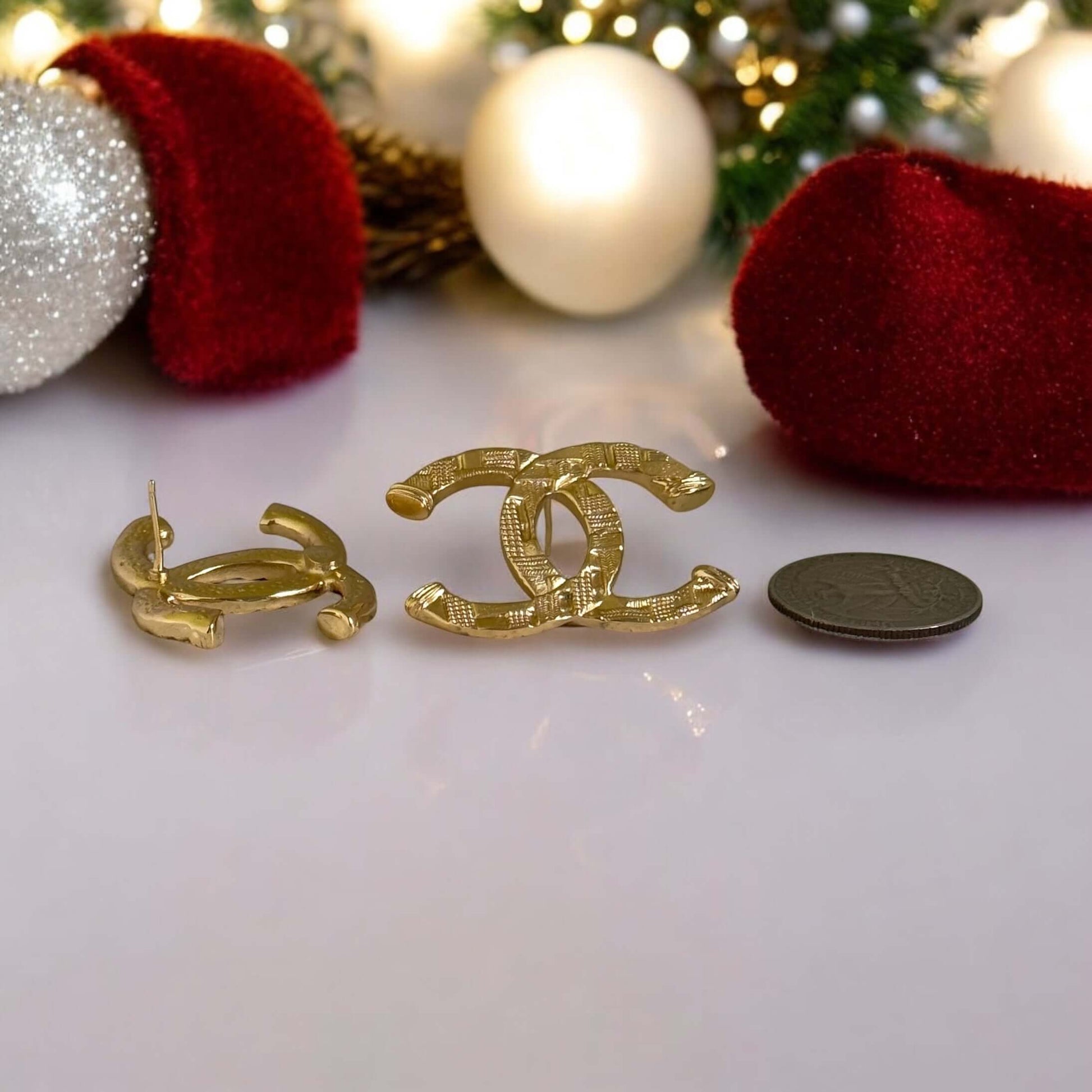 Authentic Chanel gold textured CC pre-owned earrings displayed beside a coin for size reference, festive background.