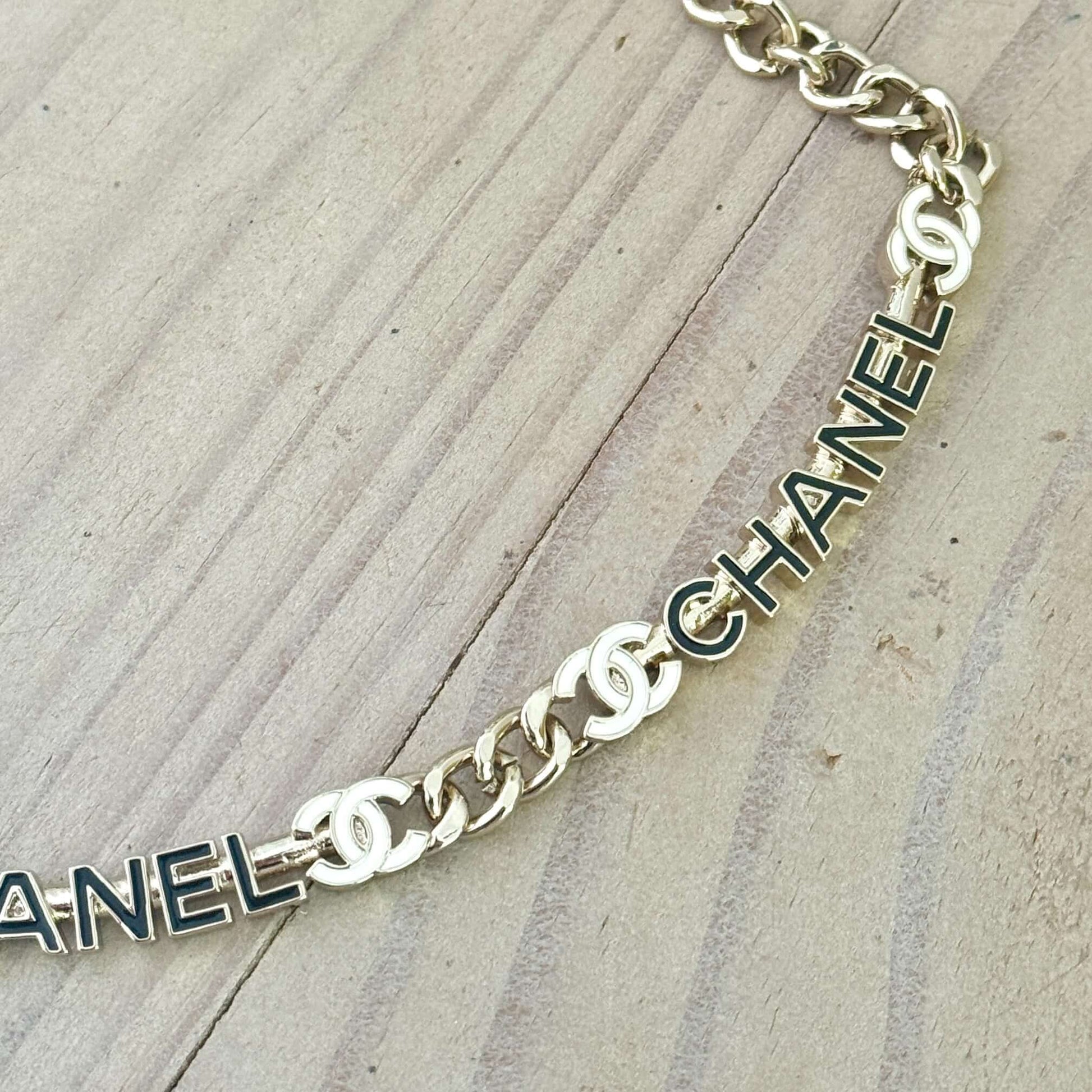 Chanel Strass Chain Adjustable Choker with elegant black and white name pendants and gold chain on a wooden surface.