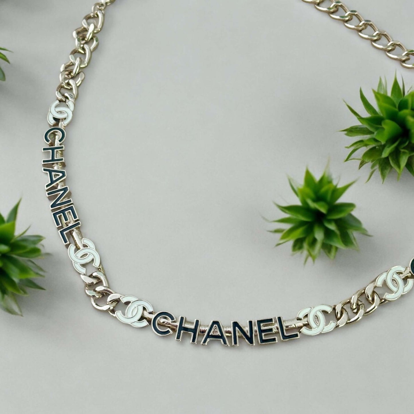 Chanel Strass Chain Adjustable Choker with elegant black and white cut name pendants on a light background, surrounded by green plants.