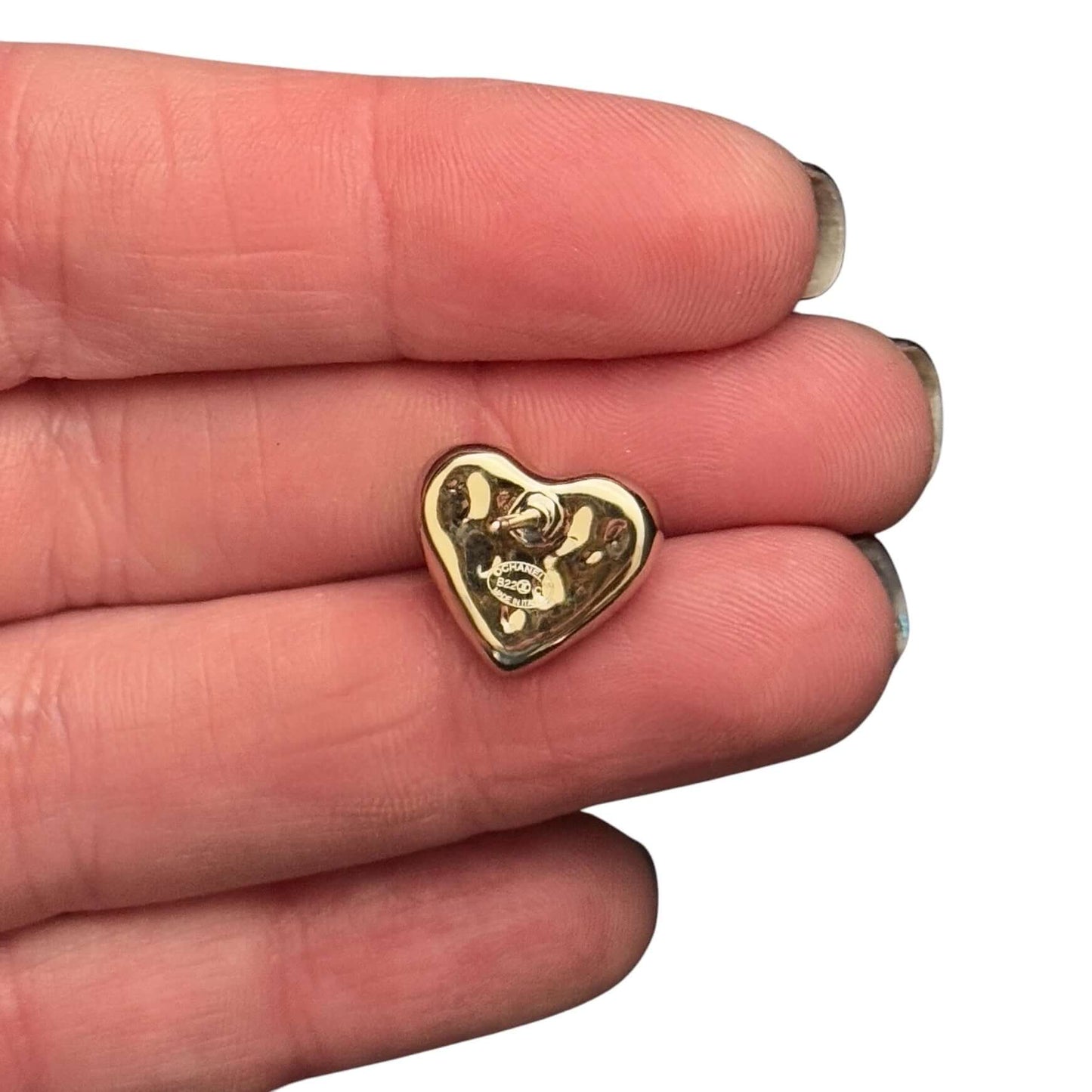 Hand holding a gold plated heart charm with an engraved logo, showcasing its shiny surface and unique design.