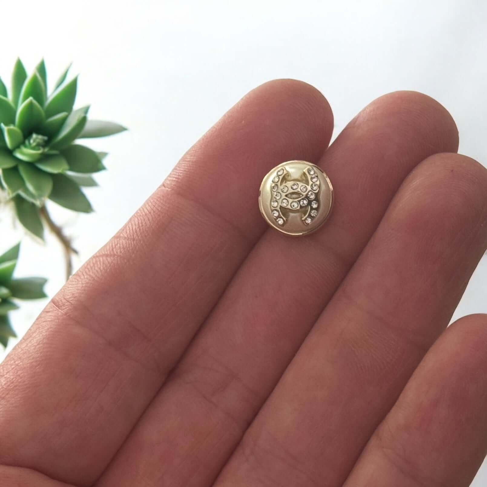 Person holding a small gold button with an intricate turtle design and clear crystals