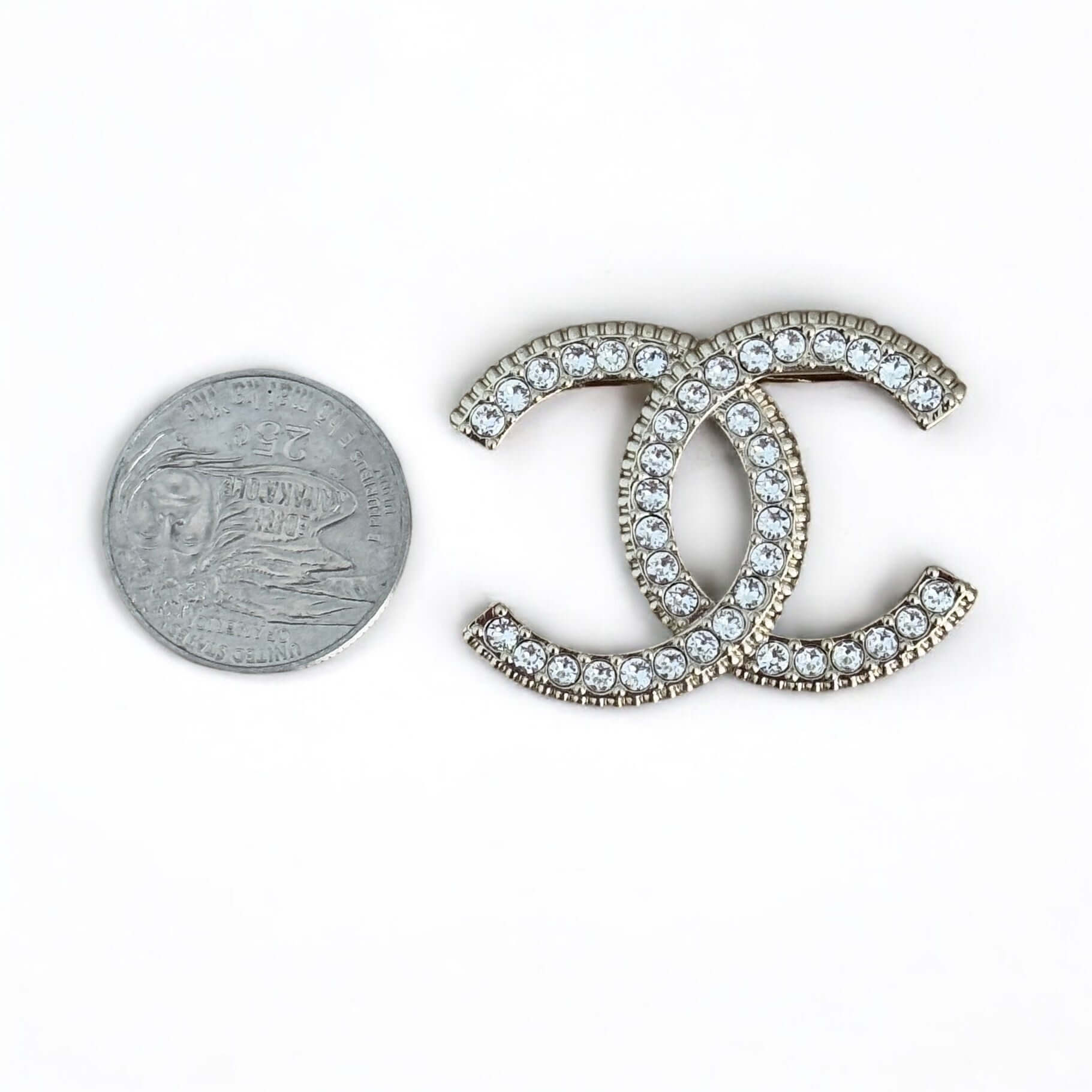 Pre-owned Chanel lighter brooch with CC design and crystals, alongside a quarter for size reference.