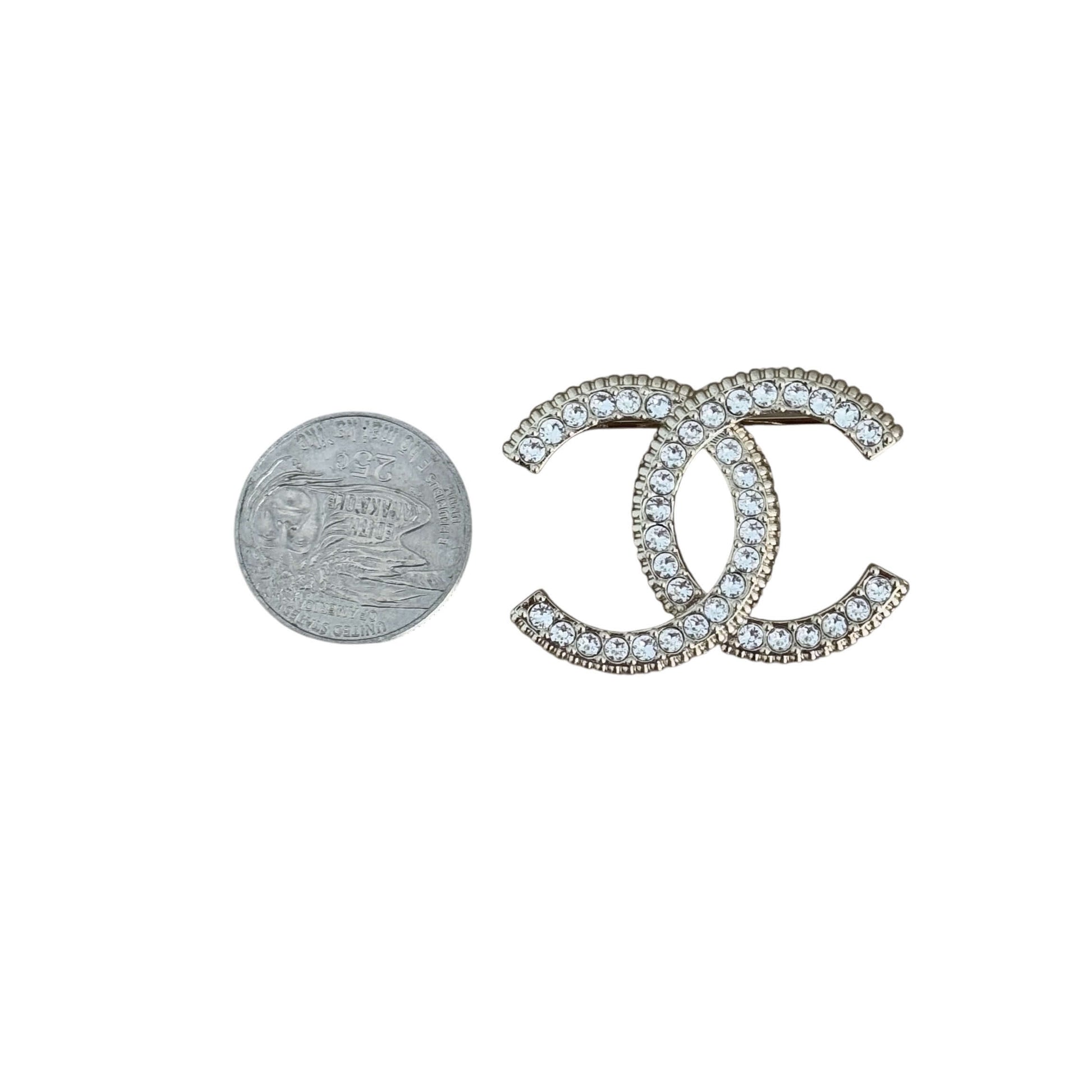 Pre-owned Chanel lighter brooch with gold and crystal CC design, showcasing size next to a quarter for scale.