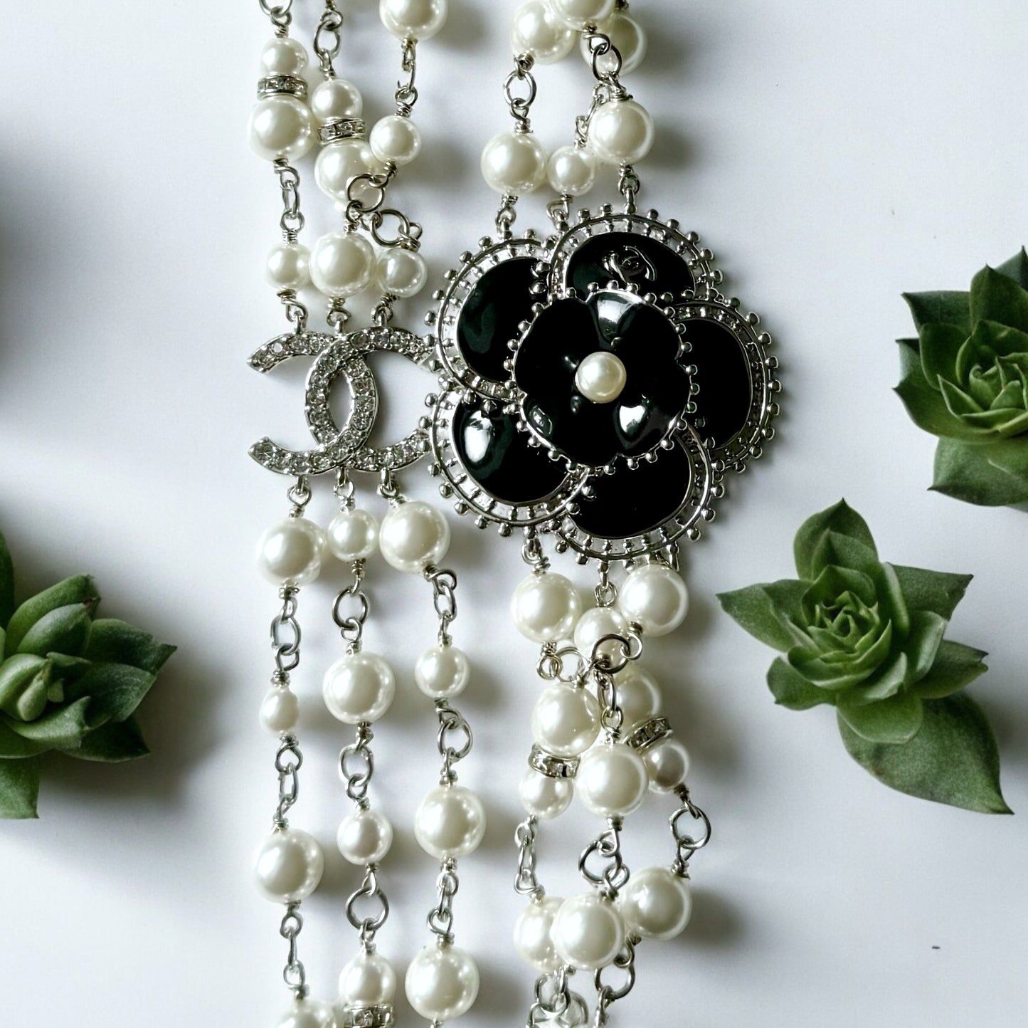 Chanel Pearl Camila Enamel Flower Three Strand NecklaceGorgeous Authentic Chanel Triple Strand (faux) Pearl linked with silver wiring , Double C with crystals Link , Black with silver accents enamel Camila Flower Focal Point Charm Lobster Safety Clasp Mar