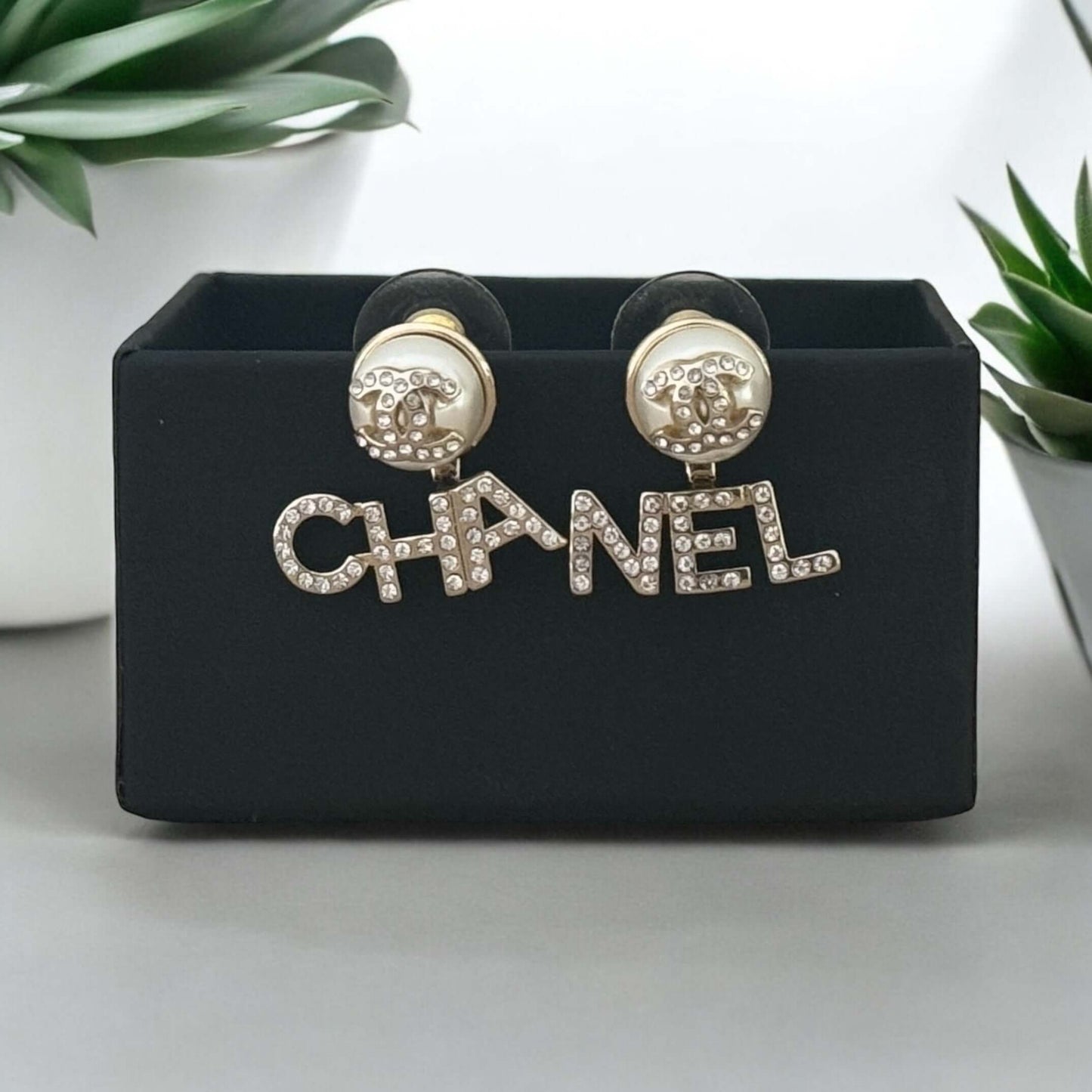 Chanel iconic gold earrings with clear crystals, off-white enamel CC center, "CHA" and "NEL" on each side, on display with gift box. My Mama Found What 